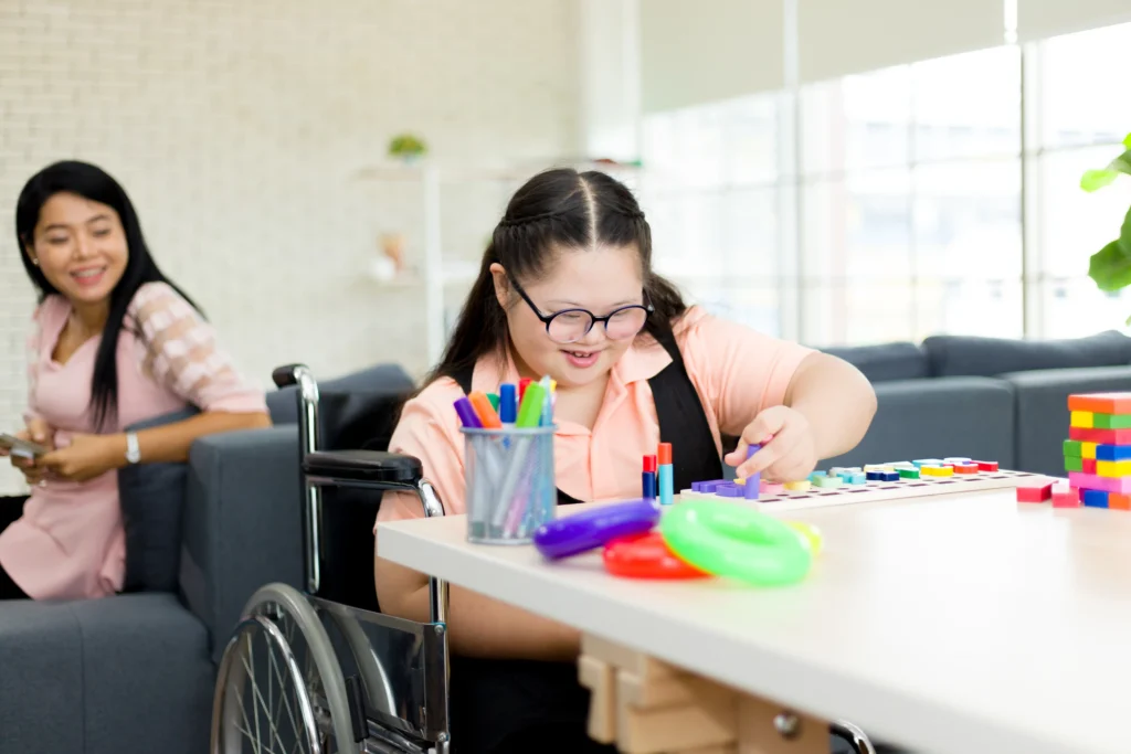 A young girl in a wheelchair drawing at a table with art supplies.