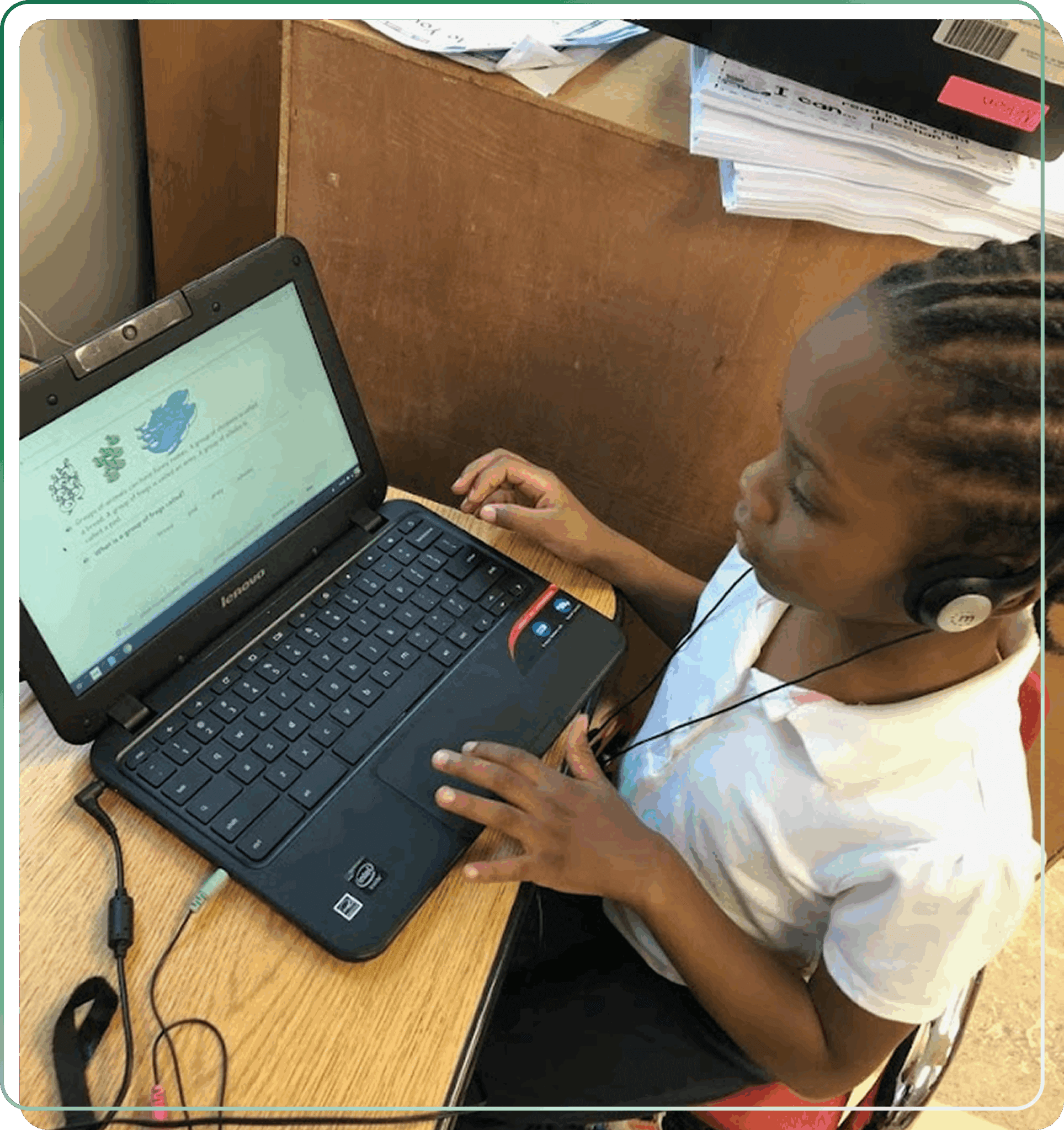 A young girl using a laptop at a desk, wearing earphones.